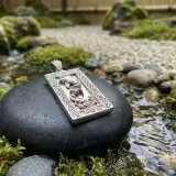 Ciondolo con drago, emblema della fortuna, adagiato su una pietra in un giardino zen con acqua corrente.