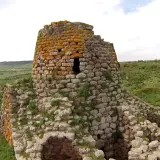 Il nuraghe Santa Barbara, con la sua torre in pietra ricoperta di licheni arancioni, domina un paesaggio verdeggiante e collinare.