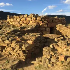 Rovine del nuraghe San Pietro, una struttura in pietra con un ingresso scuro, sotto un cielo azzurro con nuvole bianche.