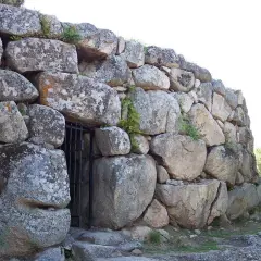 Muro imponente di un nuraghe, con un cancello in ferro che custodisce l'ingresso. Le pietre antiche, segnate dal tempo, raccontano storie millenarie.