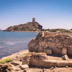 Rovine antiche sulla costa sarda, con una torre in lontananza. Un pezzo di storia della Sardegna che emerge dal passato.