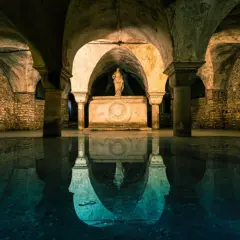 La cripta di San Marco, con le sue volte in pietra e la statua riflessa sull'acqua, evoca un'atmosfera mistica e antica.