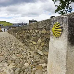 Pietra miliare con conchiglia simbolo cristiano sul Cammino di Santiago. Il selciato conduce verso un villaggio.
