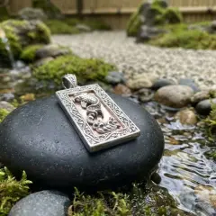 Ciondolo con drago, emblema della fortuna, adagiato su una pietra in un giardino zen con acqua corrente.