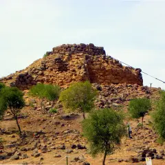 Il nuraghe Sirai, imponente struttura in pietra, si erge su un colle arido, circondato da vegetazione mediterranea.