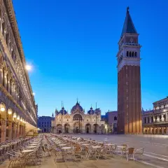 Un maestoso palazzo in Piazza San Marco, Venezia, si erge con la sua architettura imponente, mentre il cielo azzurro della sera fa da sfondo.