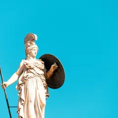 Statua di Atena, dea greca della giovinezza e della saggezza, con lancia e scudo contro un cielo azzurro.