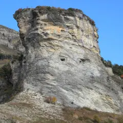 Imponente roccia con aperture che ricordano il vallo alpino del littorio. Un paesaggio montano suggestivo sotto un cielo azzurro.