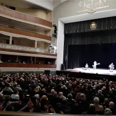 Un pubblico numeroso applaude sul palco, dove tre artisti si esibiscono in quello che potrebbe essere il primo teatro in Italia.