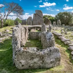 Antica tomba dei giganti di Li Lolghi, con imponenti pietre erette e un corridoio centrale, immersa nel verde sotto un cielo azzurro.