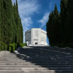 Lunga scalinata conduce all'imponente ossario di Oslavia, fiancheggiata da alti cipressi e vegetazione curata.