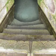 Antica scala in pietra conduce a un pozzo sacro in Sardegna, le cui acque limpide riflettono il cielo.