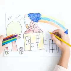 Bambino colora un disegno con matite, creando una casa, un albero e un arcobaleno. La dea Ebe, simbolo di giovinezza, ispira la creatività.