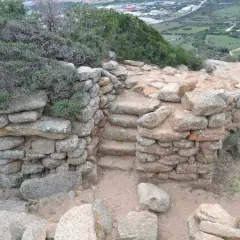 Antiche pietre del nuraghe Cabu Abbas, con gradini in pietra e vegetazione mediterranea.