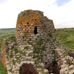 Il nuraghe Santa Barbara, con la sua torre in pietra ricoperta di licheni arancioni, domina un paesaggio verdeggiante e collinare.