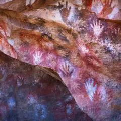 Antiche pitture rupestri nella grotta delle mani, con impronte di mani rosse e bianche su roccia.