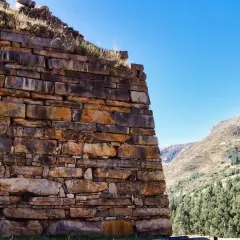 Antiche mura di pietra a Chavin de Huantar, con montagne verdi e cielo azzurro sullo sfondo.