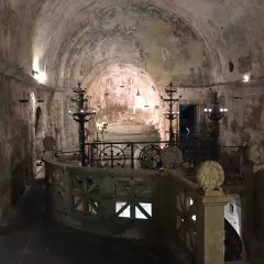 Interno della cripta di Santa Cristina, con affreschi antichi, candelabri e un sarcofago.