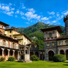 Cortile di un complesso architettonico con torre, affreschi e un pozzo, immerso nel verde. Sembra un luogo avvolto da un'aura di mistero, quasi una rosazza esoterica.