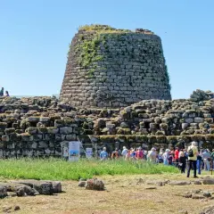 Un imponente complesso di nuraghi sardegna domina il paesaggio, con visitatori che esplorano le antiche rovine sotto un cielo azzurro.