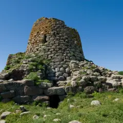 Il nuraghe Santa Barbara a Villanova Truschedu, imponente struttura in pietra con vegetazione rigogliosa, si erge sotto un cielo azzurro.