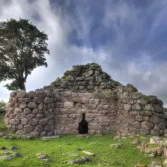 Il nuraghe Appiu, con la sua imponente struttura in pietra, si erge solitario sotto un cielo nuvoloso, testimone di antiche storie.