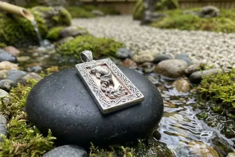 Ciondolo con drago, emblema della fortuna, adagiato su una pietra in un giardino zen con acqua corrente.