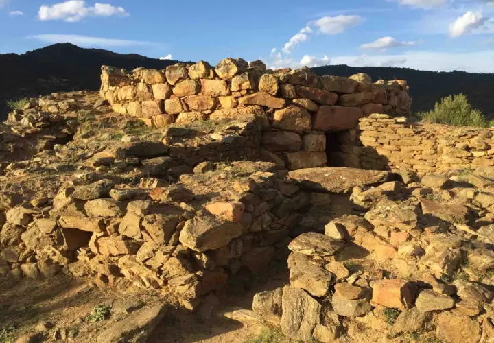 Rovine del nuraghe San Pietro, una struttura in pietra con un ingresso scuro, sotto un cielo azzurro con nuvole bianche.