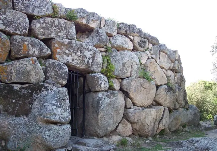 Muro imponente di un nuraghe, con un cancello in ferro che custodisce l'ingresso. Le pietre antiche, segnate dal tempo, raccontano storie millenarie.