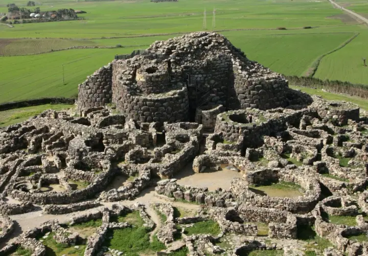 Antica fortezza nuragica in pietra, con torri e mura a vista, immersa in un paesaggio rurale verdeggiante. I nuraghi dove si trovano sono testimoni di un passato millenario.