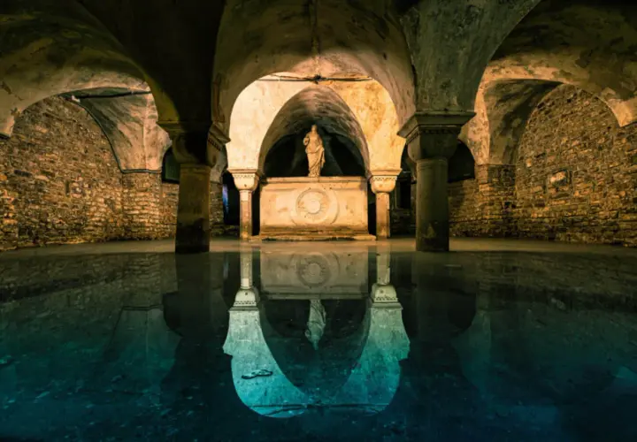 La cripta di San Marco, con le sue volte in pietra e la statua riflessa sull'acqua, evoca un'atmosfera mistica e antica.