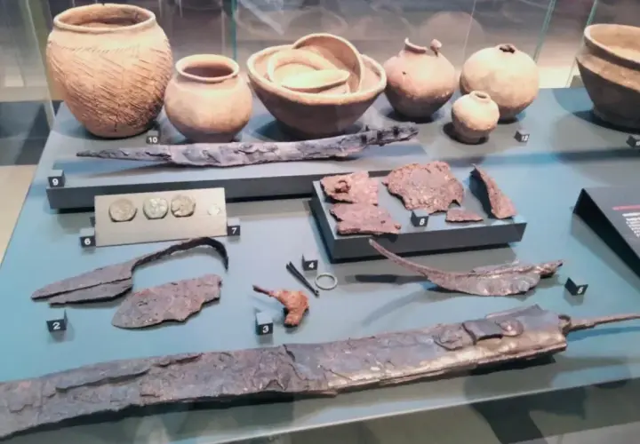 Reperti archeologici, tra cui vasi, monete e armi, simili a quelli della patera di Parabiago, esposti in un museo.