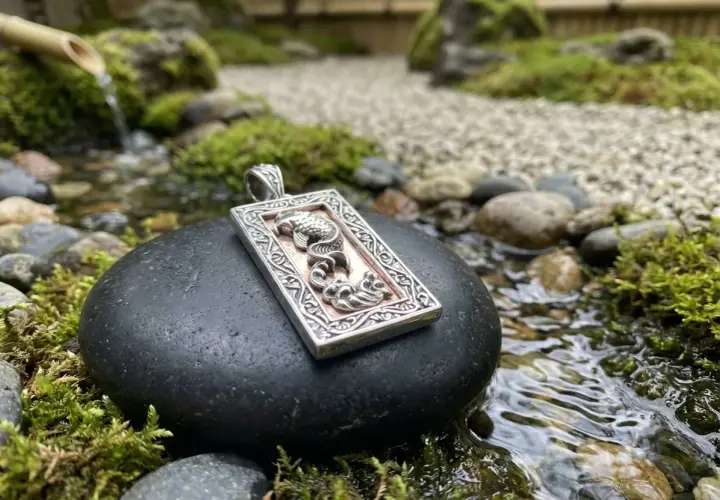 Ciondolo con drago, emblema della fortuna, adagiato su una pietra in un giardino zen con acqua corrente.