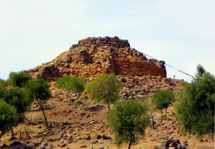 Il nuraghe Sirai, imponente struttura in pietra, si erge su un colle arido, circondato da vegetazione mediterranea.