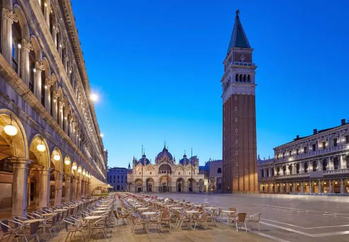Un maestoso palazzo in Piazza San Marco, Venezia, si erge con la sua architettura imponente, mentre il cielo azzurro della sera fa da sfondo.