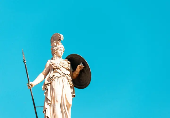 Statua di Atena, dea greca della giovinezza e della saggezza, con lancia e scudo contro un cielo azzurro.
