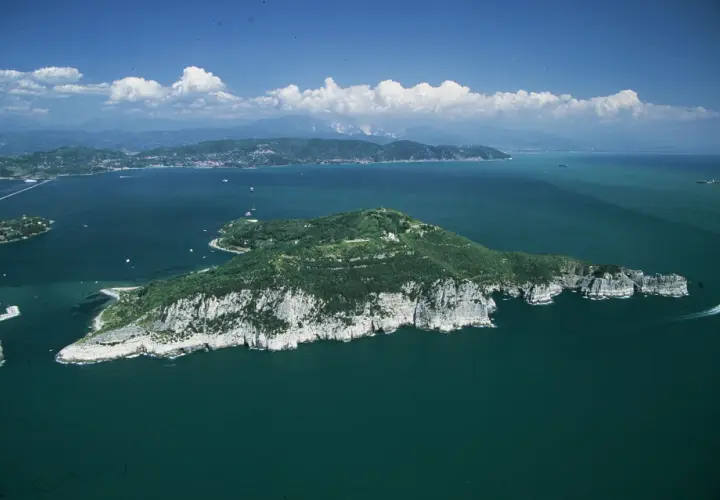 Isola verdeggiante con scogliere bianche, mare blu intenso e nuvole bianche. Si intravede la **grotta dei colombi** tra le rocce.