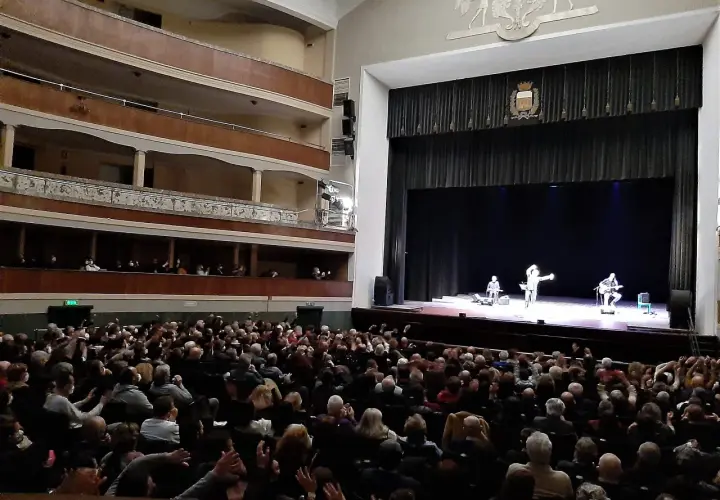 Un pubblico numeroso applaude sul palco, dove tre artisti si esibiscono in quello che potrebbe essere il primo teatro in Italia.