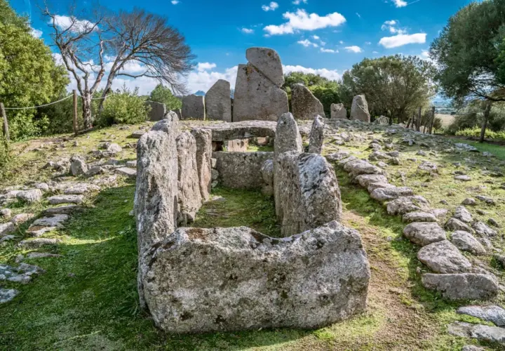 Antica tomba dei giganti di Li Lolghi, con imponenti pietre erette e un corridoio centrale, immersa nel verde sotto un cielo azzurro.