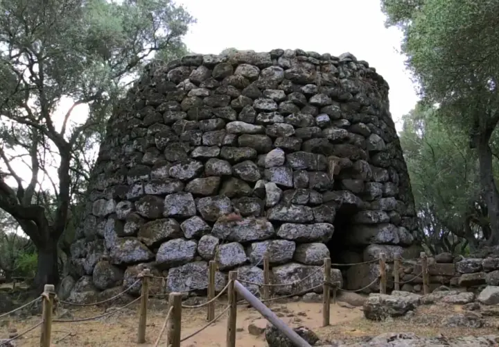 Antico nuraghe di Santa Cristina a Paulilatino, imponente struttura in pietra con un ingresso buio, circondato da alberi secolari.