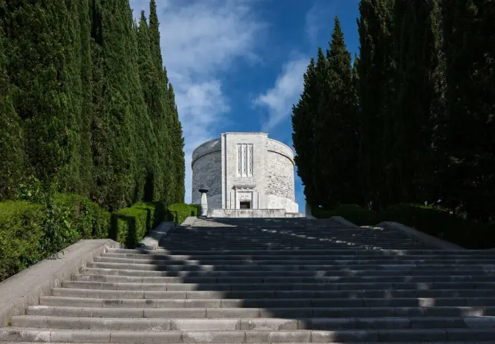 Lunga scalinata conduce all'imponente ossario di Oslavia, fiancheggiata da alti cipressi e vegetazione curata.