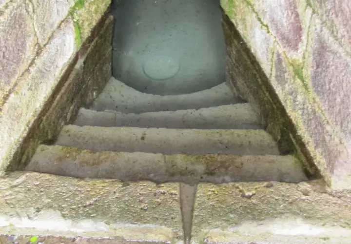 Antica scala in pietra conduce a un pozzo sacro in Sardegna, le cui acque limpide riflettono il cielo.