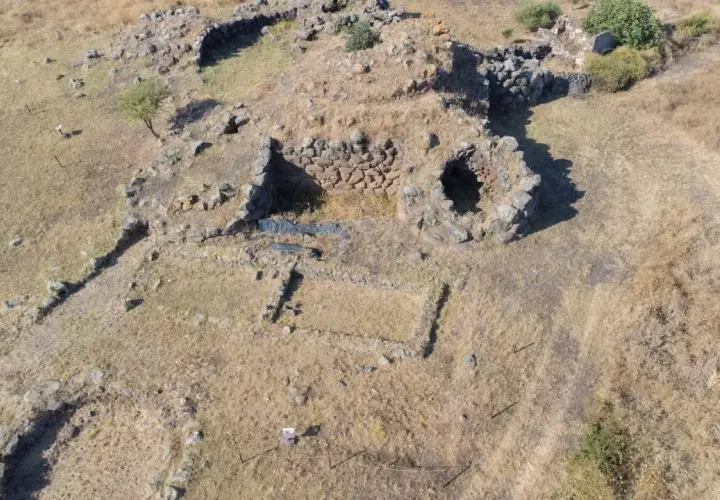 Resti di un antico villaggio nuragico, con pietre che delineano le fondamenta di antiche abitazioni e mura.
