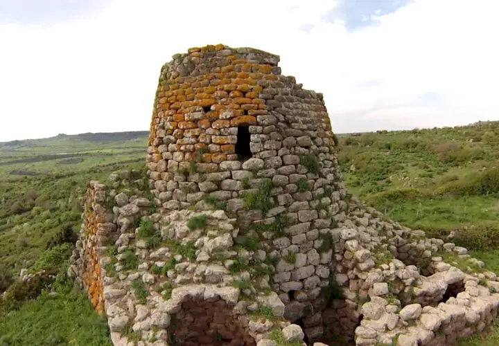 Il nuraghe Santa Barbara, con la sua torre in pietra ricoperta di licheni arancioni, domina un paesaggio verdeggiante e collinare.