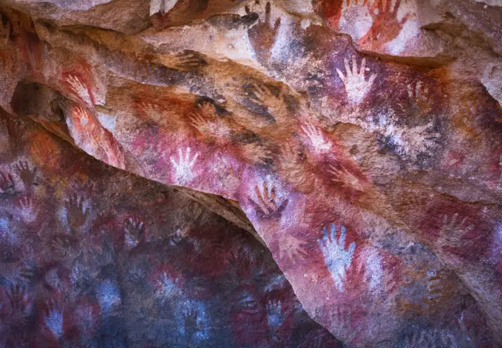 Antiche pitture rupestri nella grotta delle mani, con impronte di mani rosse e bianche su roccia.
