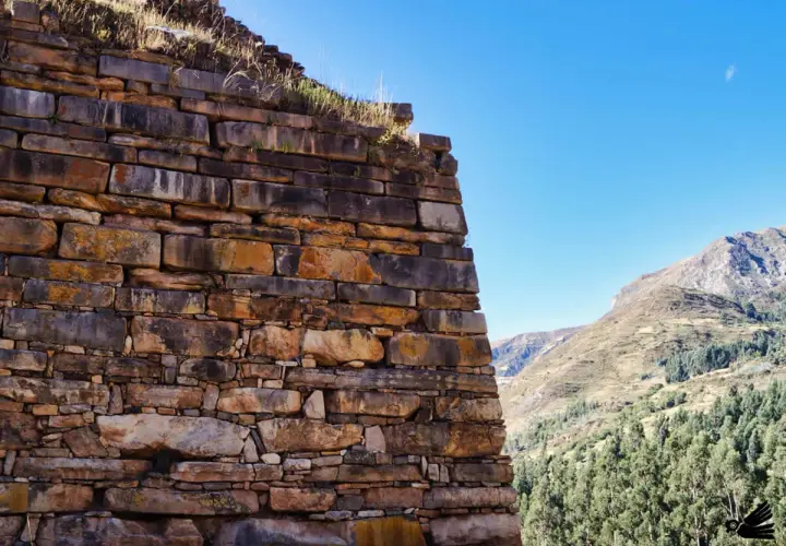 Antiche mura di pietra a Chavin de Huantar, con montagne verdi e cielo azzurro sullo sfondo.