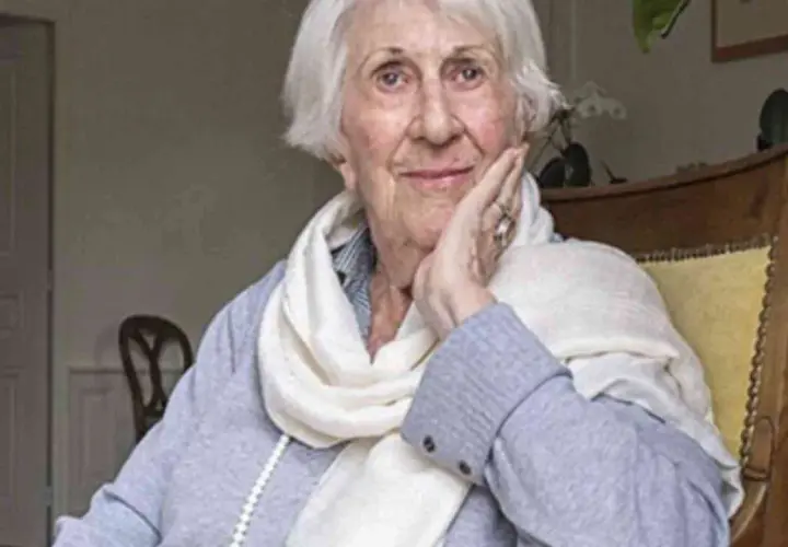 Annick de Souzenelle, con un sorriso sereno, appoggia il viso sulla mano, avvolta in una sciarpa chiara.