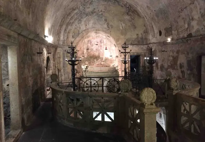 Interno della cripta di Santa Cristina, con affreschi antichi, candelabri e un sarcofago.