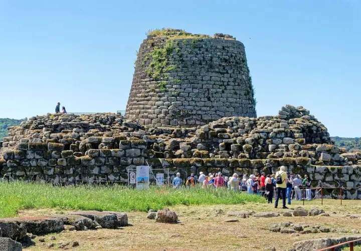 Un imponente complesso di nuraghi sardegna domina il paesaggio, con visitatori che esplorano le antiche rovine sotto un cielo azzurro.