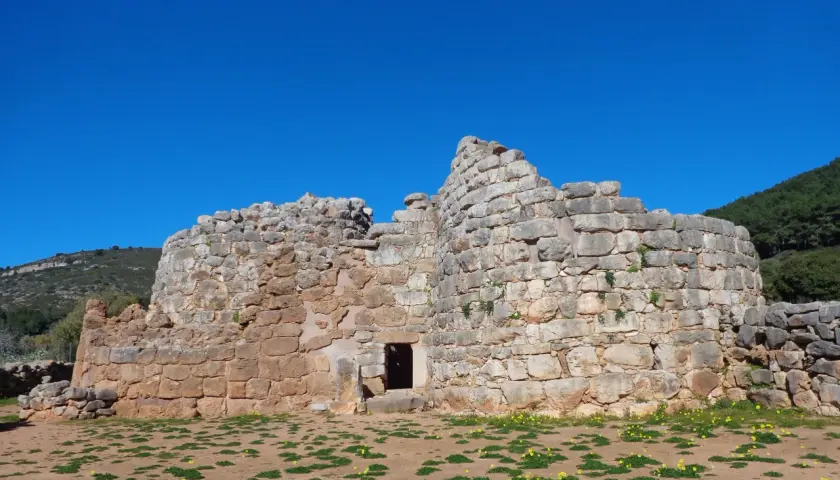 Il nuraghe Palmavera, imponente struttura in pietra sotto un cielo azzurro, testimone di antiche civiltà.